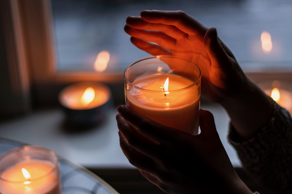 hand holding lit candle with other lit candles in the room
